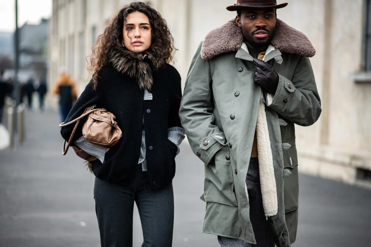Topshop хоче повернутися на вершину. Британський ритейлер запускає інтернет-магазин, який буде доступний у 23 країнах. На фото зображена стильно одягнена пара, яка йде міською вулицею – жінка в чорному пальто з хутряним коміром та шкіряною сумкою, а чоловік в оливковій паркі з хутряною підкладкою та капелюхом – міський вуличний стиль.