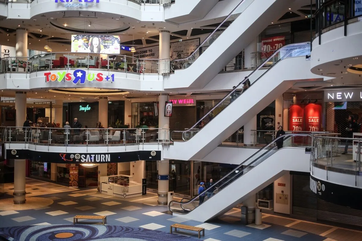 Довге майбутнє Blue City. Багаторівневий інтер'єр торговельного центру Blue City у Варшаві з ескалаторами, скляними балюстрадами та видимими магазинами, включаючи Saturn та Toys “R” Us, у робочі години.