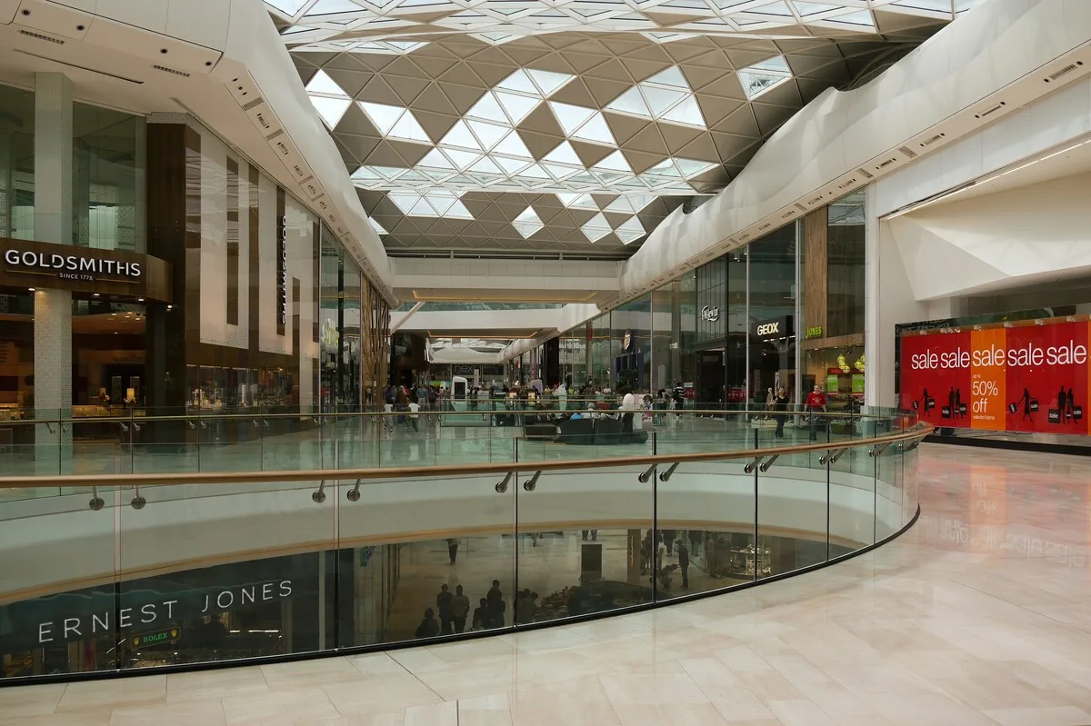 Реконструкція Alfa Centrum у Гданську. Інтер'єр сучасного торгового центру має скляний дах, торгові аркади та видимі магазини з обох боків, на тлі яких покупці роблять покупки.