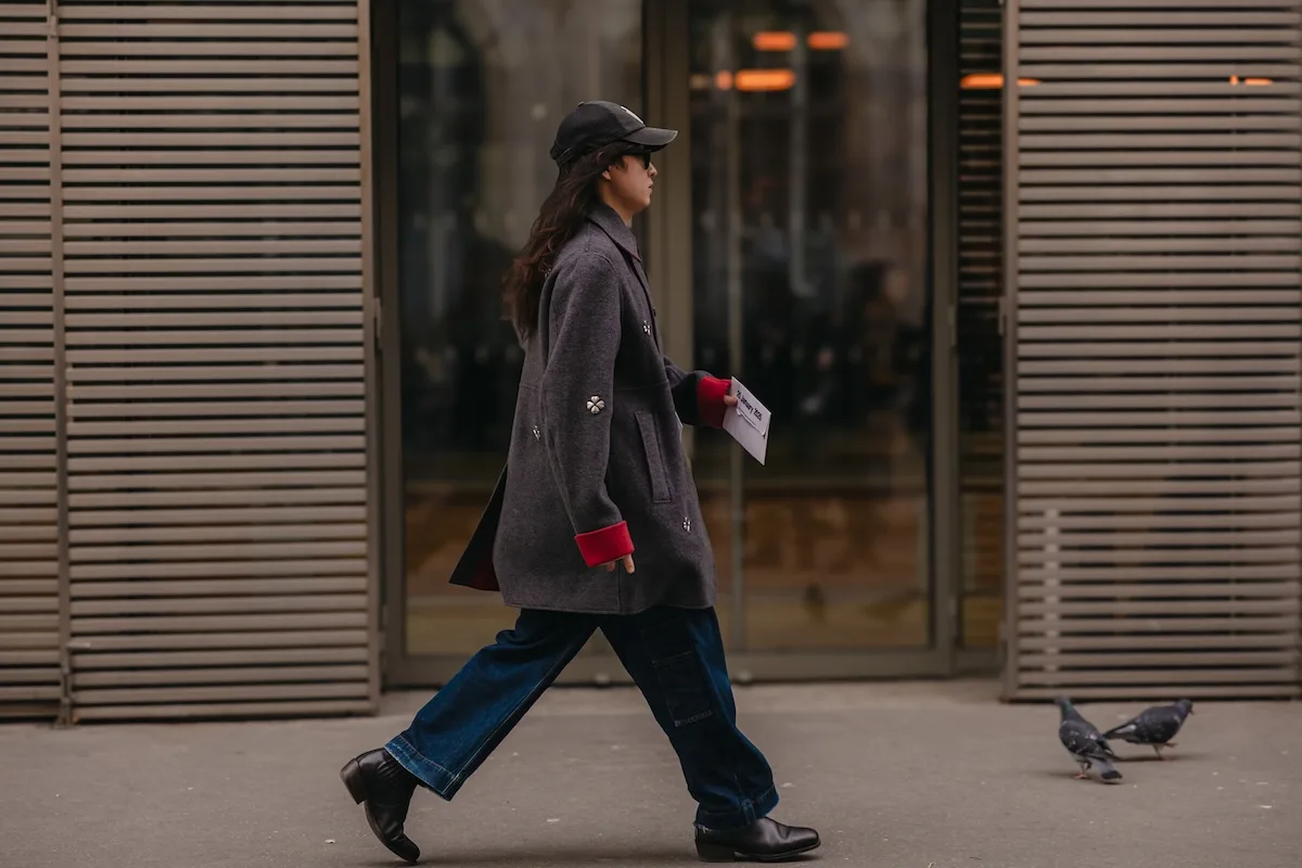 Людина в сірому пальто та джинсах йде міською вулицею.