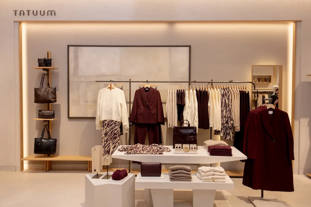 Інтер'єр магазину Tatuum з елегантною вітриною жіночого одягу в приглушених кольорах – куртки, светри, сукні та сумочки, розкладені на вішалках та столах.