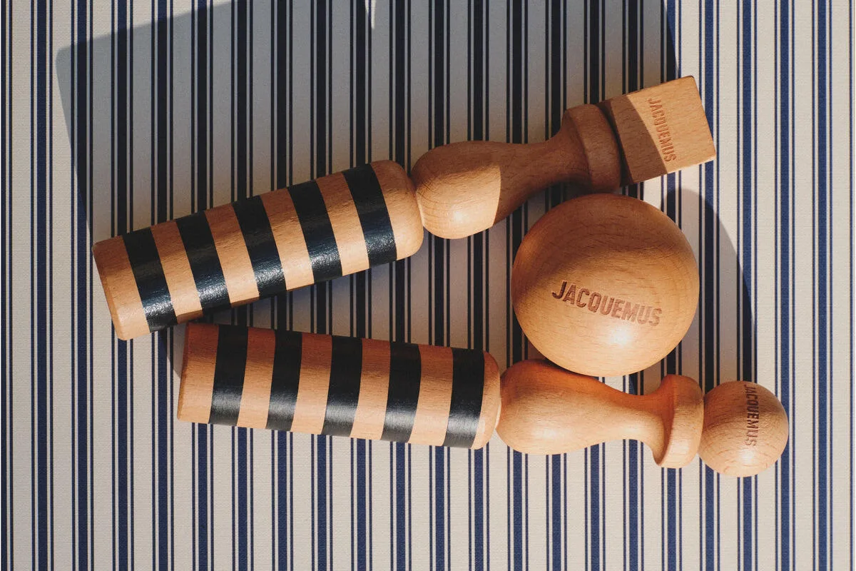 Предмети Jacquemus. На фото: Дерев'яний набір для боулінгу Jacquemus з кулею та трьома кеглями на смугастому фоні.
