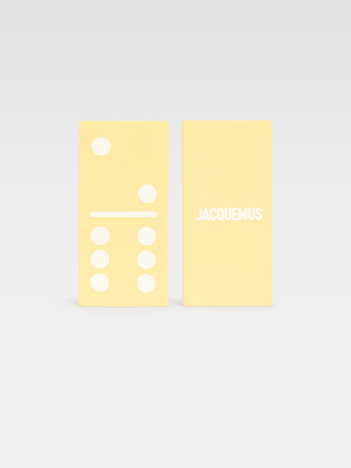 Жовті доміно Jacquemus з білими цятками та логотипом бренду на однотонному фоні.