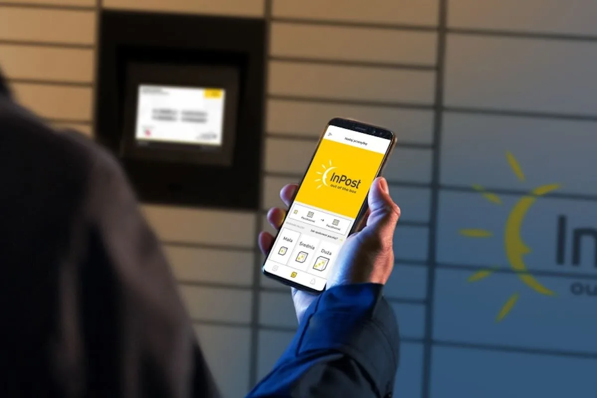 Крупний план людини, яка тримає телефон з великим жовтим логотипом InPost, стоячи перед поштовим ящиком