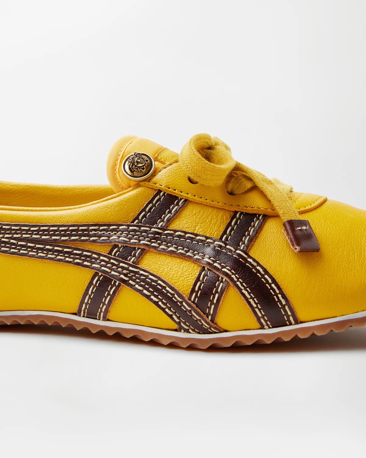 Жовті кросівки з колекції Onitsuka Tiger x Versace з коричневими смужками та контрастною строчкою. На язичку видно золоту емблему Медузи, що підтримує вінтажну естетику.