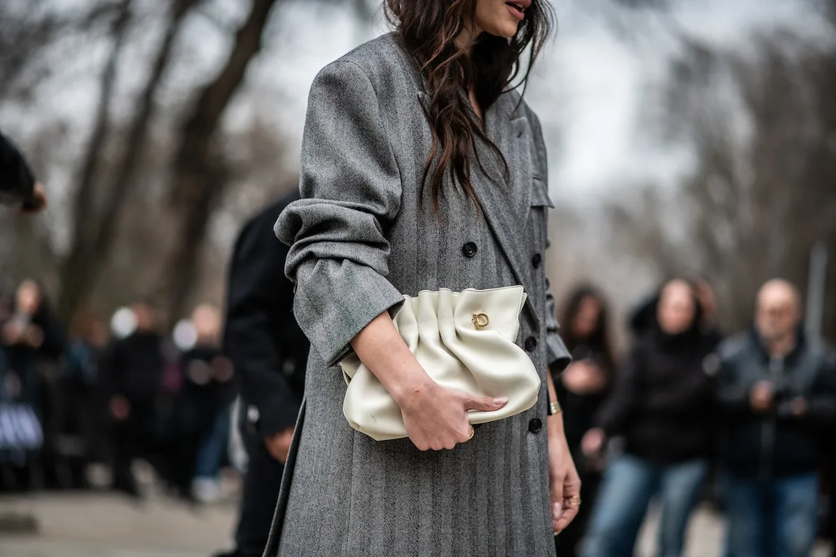 Жінка в елегантній сумці-клатчі та мінімалістичному пальто на заході вуличної моди. Фото натякає на зміни в правилах ЄС, які можуть вплинути на доступність та ціни на модні товари, імпортовані з-за меж ЄС.