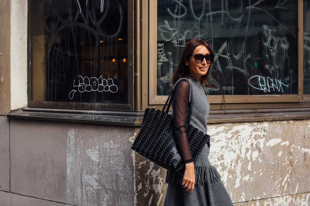 Чистий четвер 2026 – Чи відкриті магазини? Стильна жінка йде вулицею в облягаючій сукні та великих сонцезахисних окулярах, тримаючи дизайнерську сумку. Це типова міська прогулянка, особливо в передсвятковий період, коли багато людей перевіряють, чи працюють магазини у Чистий четвер 2026 року.