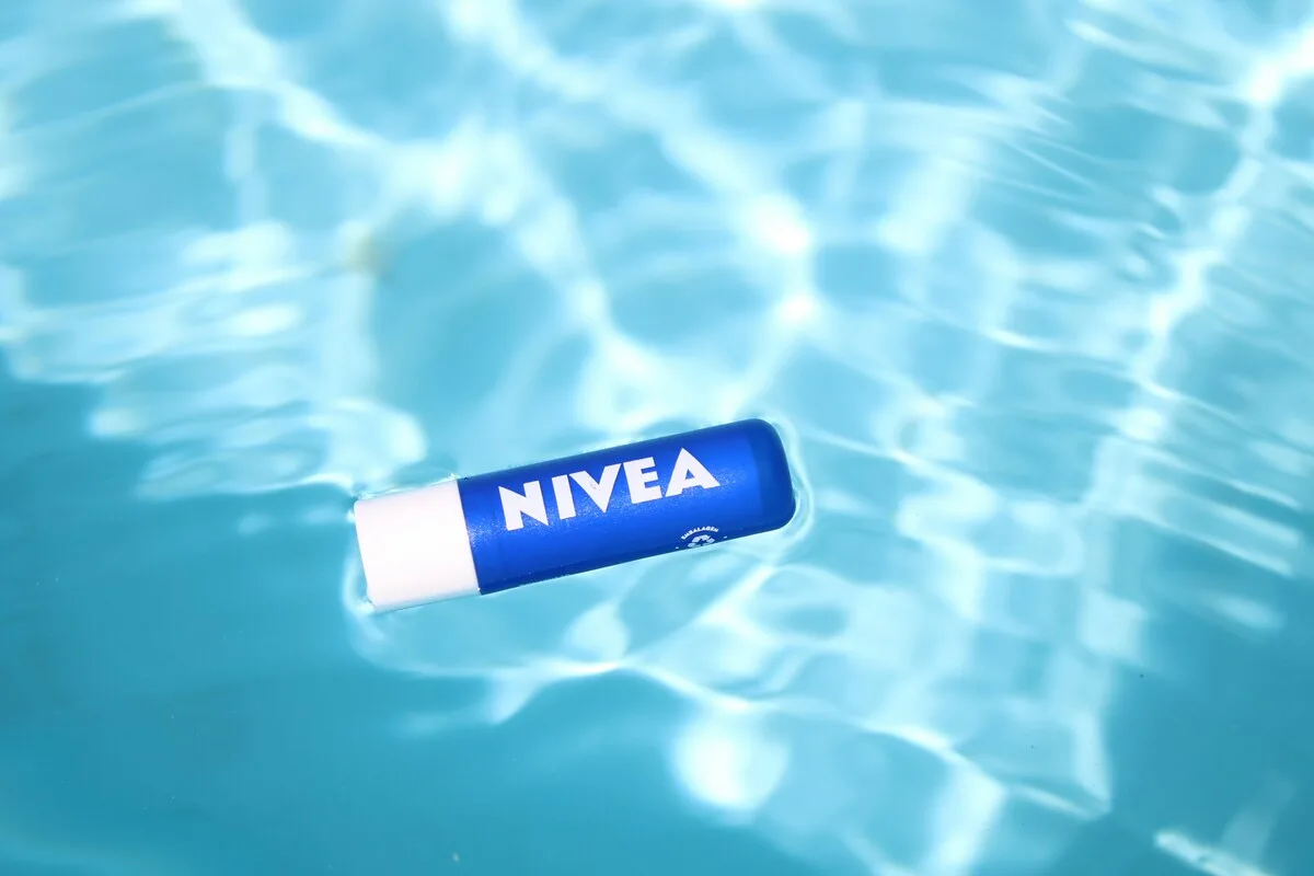 Бальзам для губ Nivea плаває на поверхні води, натякаючи на турботливий характер продукції бренду. Ілюстрація контрастує з темою статті, яка стосується фінансових проблем та заборгованості з платежами, а не самої косметики.