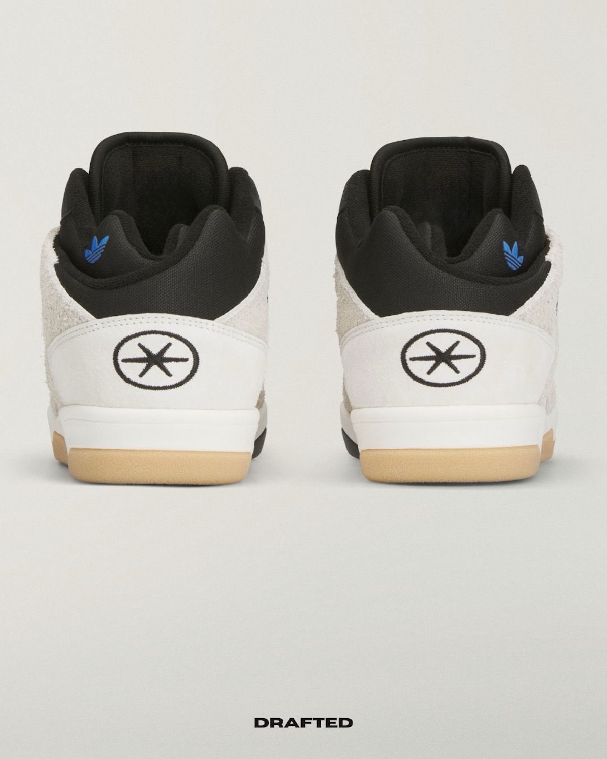 Мінімалістичні кросівки adidas x Bad Bunny чорно-білого кольору видно ззаду, з фірмовим символом каблука та ніжними синіми деталями всередині. Сира естетика та контрастні матеріали відповідають тренду експериментальних колаборацій весни 2026 року, де класика поєднується з художнім відтінком.