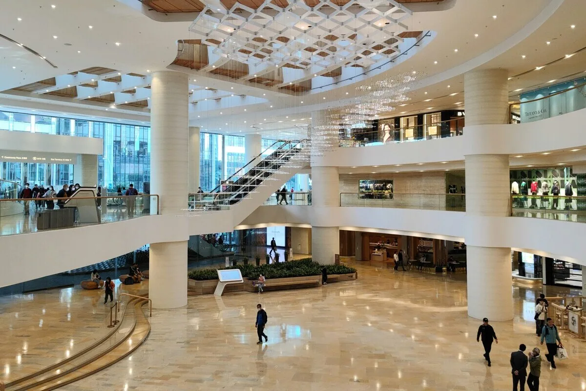 Колишня будівля Galeria Plaza у Кракові. Просторий, сучасний інтер'єр багаторівневого торгового центру вирізняється високою стелею, великими білими колонами, ескалаторами та геометричною освітлювальною інсталяцією, підвішеною над відкритим атріумом. Мармурова підлога та балкони галереї відкривають простір для прогулянок та вітрини магазинів.