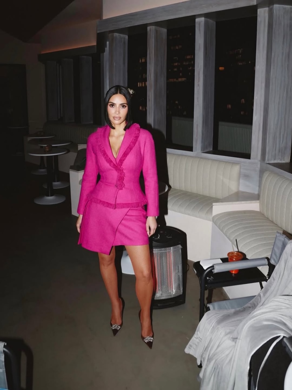 Кім Кардаш'ян у яскраво-рожевому ансамблі з короткою спідницею, сфотографована в просторі, що нагадує знімальний майданчик. Образ був включений до аукціону Kardashian Kloset, який підтримує організації, що надають безкоштовну правову допомогу.