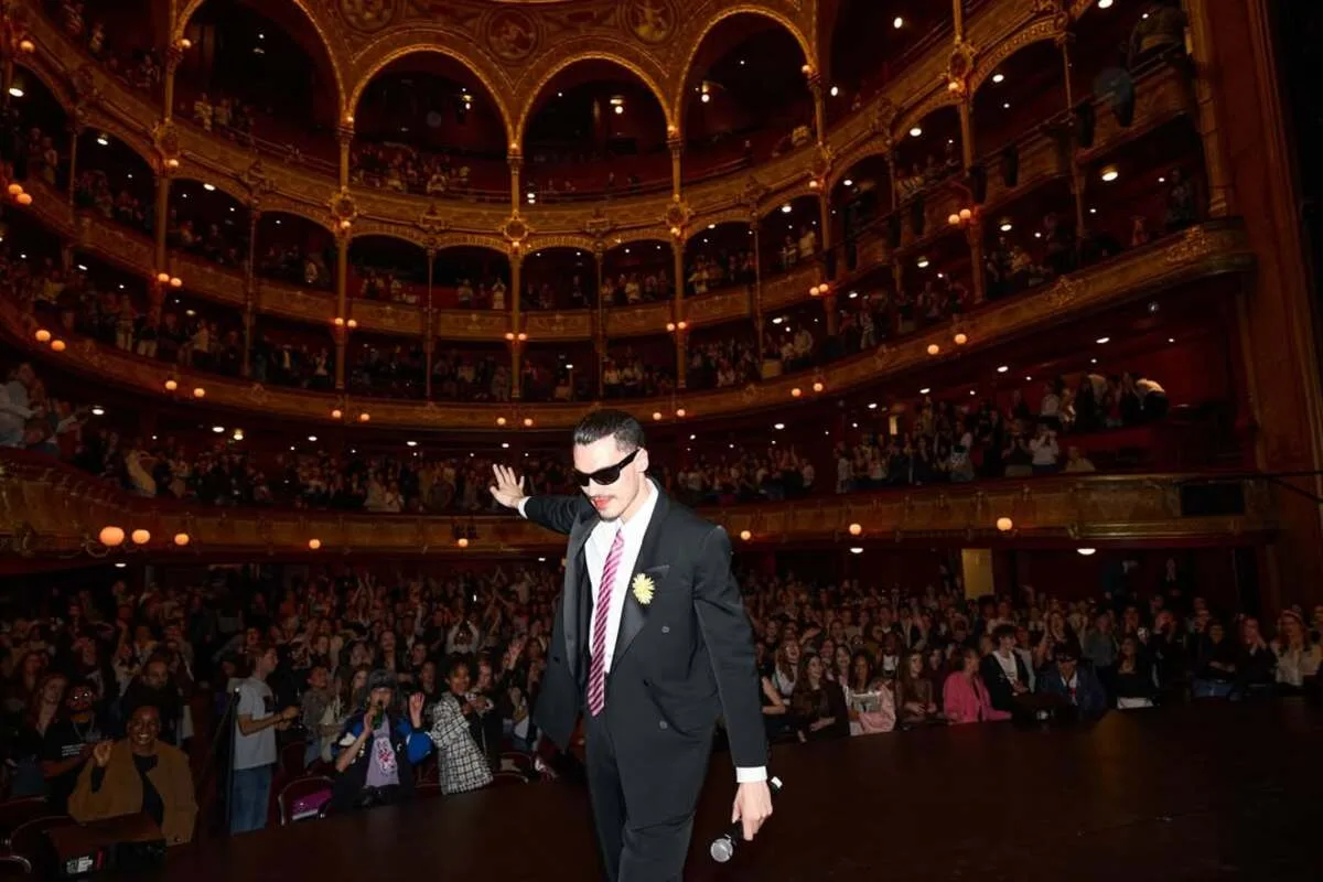 Хто такий Ліас? Що таке вечірка «La Watch Party»? На фото: Ліас (Еліас Медіні) на сцені елегантного театру під час вечірки «La Watch Party», вітаючи публіку, що зібралася на балконах та в актовій залі.