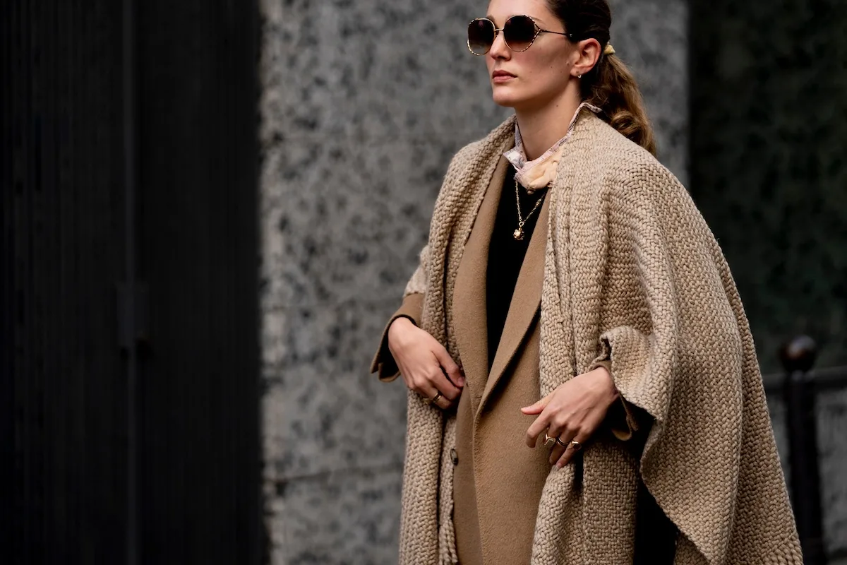 Одягнена в багатошаровий одяг бежевих та коричневих відтінків, жінка демонструє спокійний, позачасовий стиль з товстим шарфом та пальто. Це нагадує атмосферу спокійнішого дня, і багато хто задається питанням, чи є Великий четвер 2026 року вихідним з роботи та як планувати свій час.