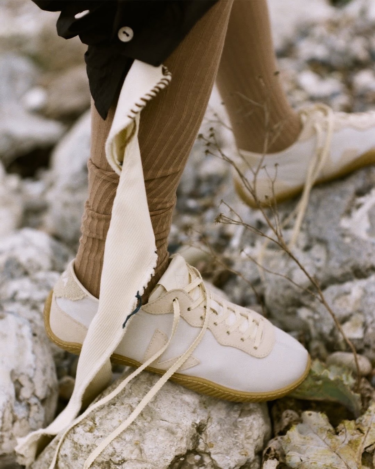 Кросівки Veja x Baserange у натуральному кремовому кольорі представлені на гальковій поверхні, з довгими шнурками та ніжними матеріалами. Ця весняна співпраця 2026 року підкреслює органічний підхід до дизайну, поєднуючи комфорт з мінімалістичною естетикою.