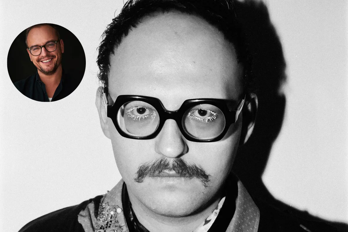 Інтерв'ю з Губертом Пельцем. Крупний план чорно-білого портрета чоловіка в товстих окулярах з геометричним малюнком і вусами, який дивиться прямо в камеру. Він одягнений у сорочку з декоративним коміром та вишивкою бісером, а також шарф, пов'язаний навколо шиї. Фотографія знята в контрастному студійному освітленні.