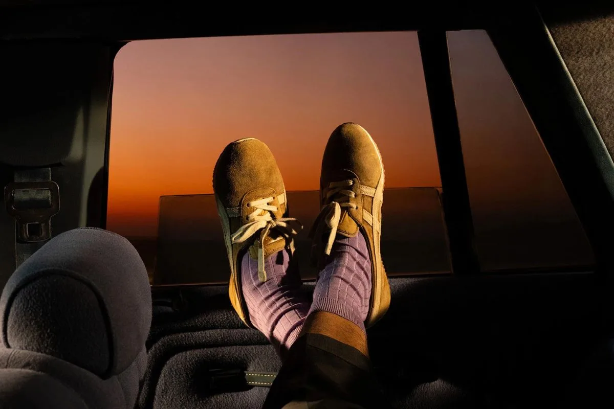 Кросівки з колекції Onitsuka Tiger x Versace. Модель TAI-CHI Sakura оливково-зеленого кольору, одягнена в машину, сфотографована на заході сонця. Тепле світло підкреслює замшеву текстуру взуття та повсякденний, лайфстайл-характер вбрання.