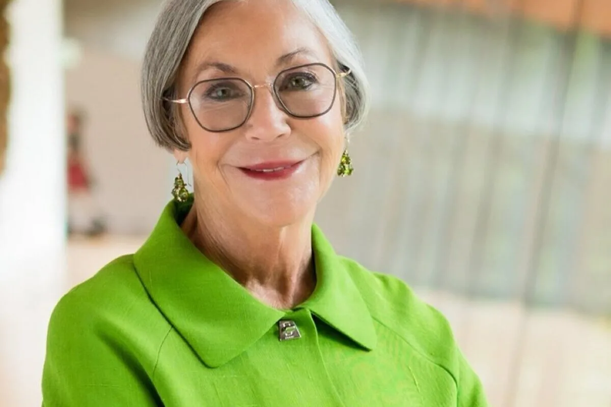 Найбагатші жінки світу 2026 року. На фотографії зображена літня жінка з коротким сивим волоссям та круглими окулярами. На ній зелений піджак з коміром та зелені сережки-підвіски. Вона злегка посміхається, і, схоже, фотографія була зроблена в яскравому, сучасному інтер'єрі з розмитим фоном.