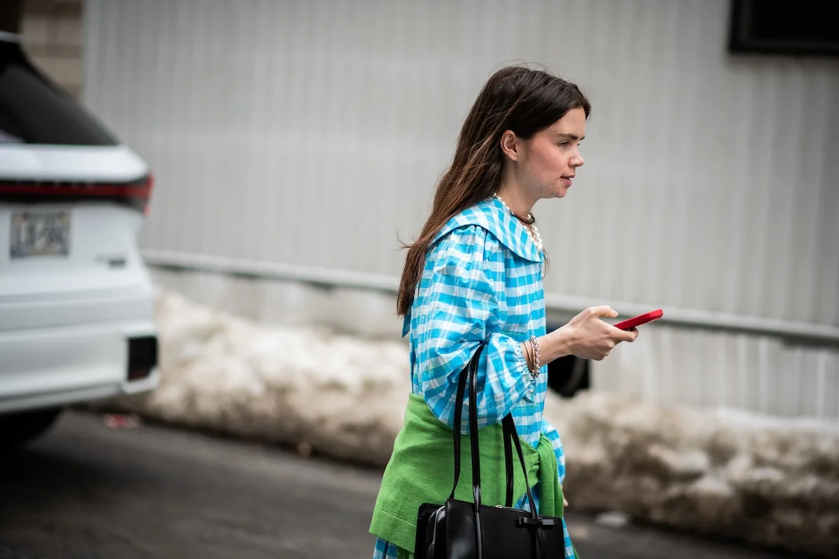 Жінка в яскравому вбранні користується смартфоном під час прогулянки містом – символ зростаючої ролі соціальної комерції у швидкій моді. Шопінг одягу все частіше відбувається онлайн та натхненний соціальними мережами. Зображення демонструє, як технології та тренди впливають на розвиток ринку швидкої моди.