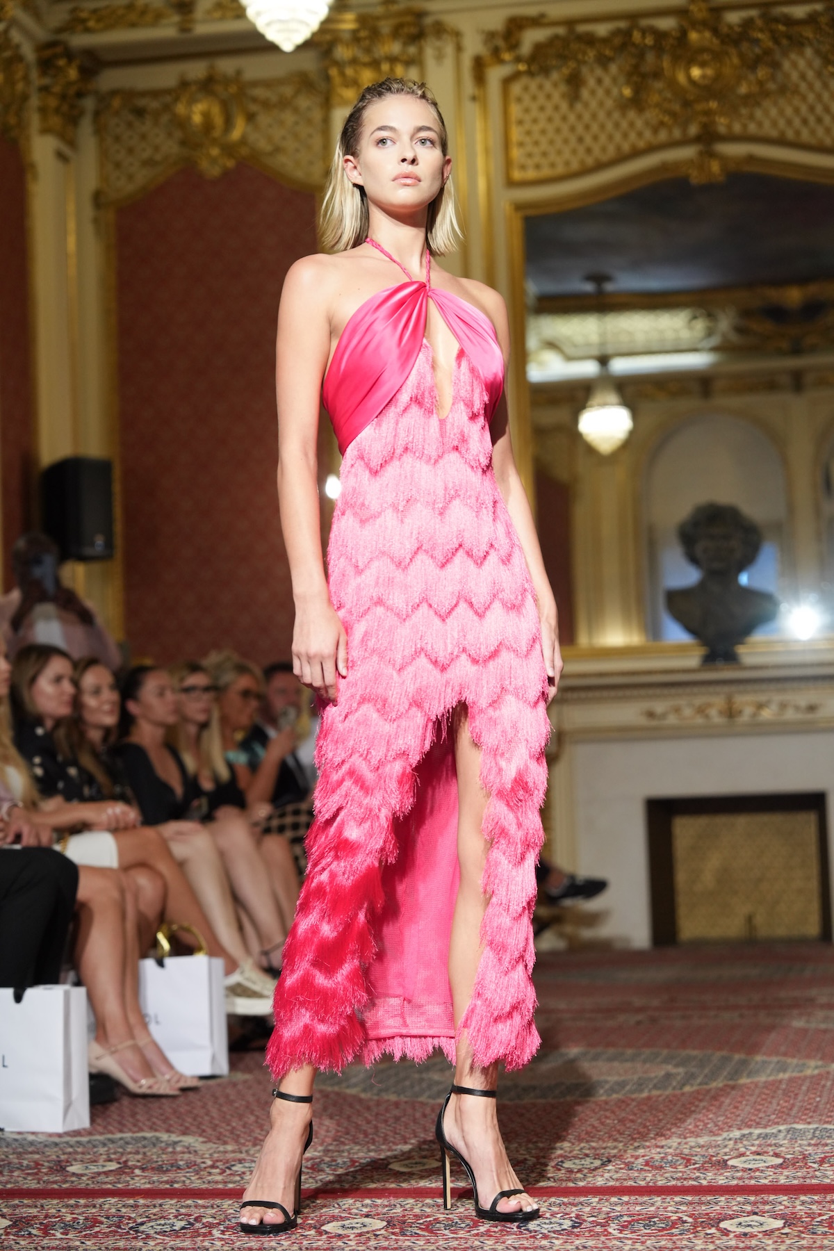 Модель на подіумі Польського дня моди в рожевій вечірній сукні з бахромою, показ мод в елегантному інтер'єрі