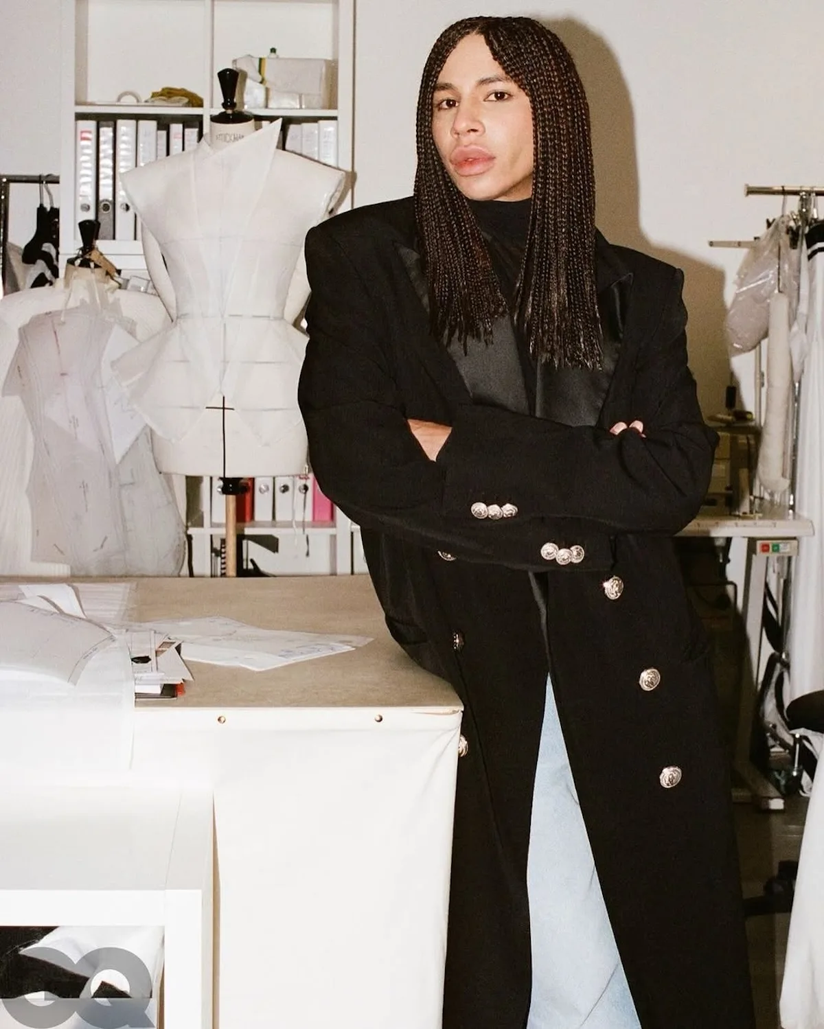 Креативний директор Balmain Олів'є Рустен у модній студії, одягнений у чорний піджак, перед манекеном та дизайнерськими ескізами.