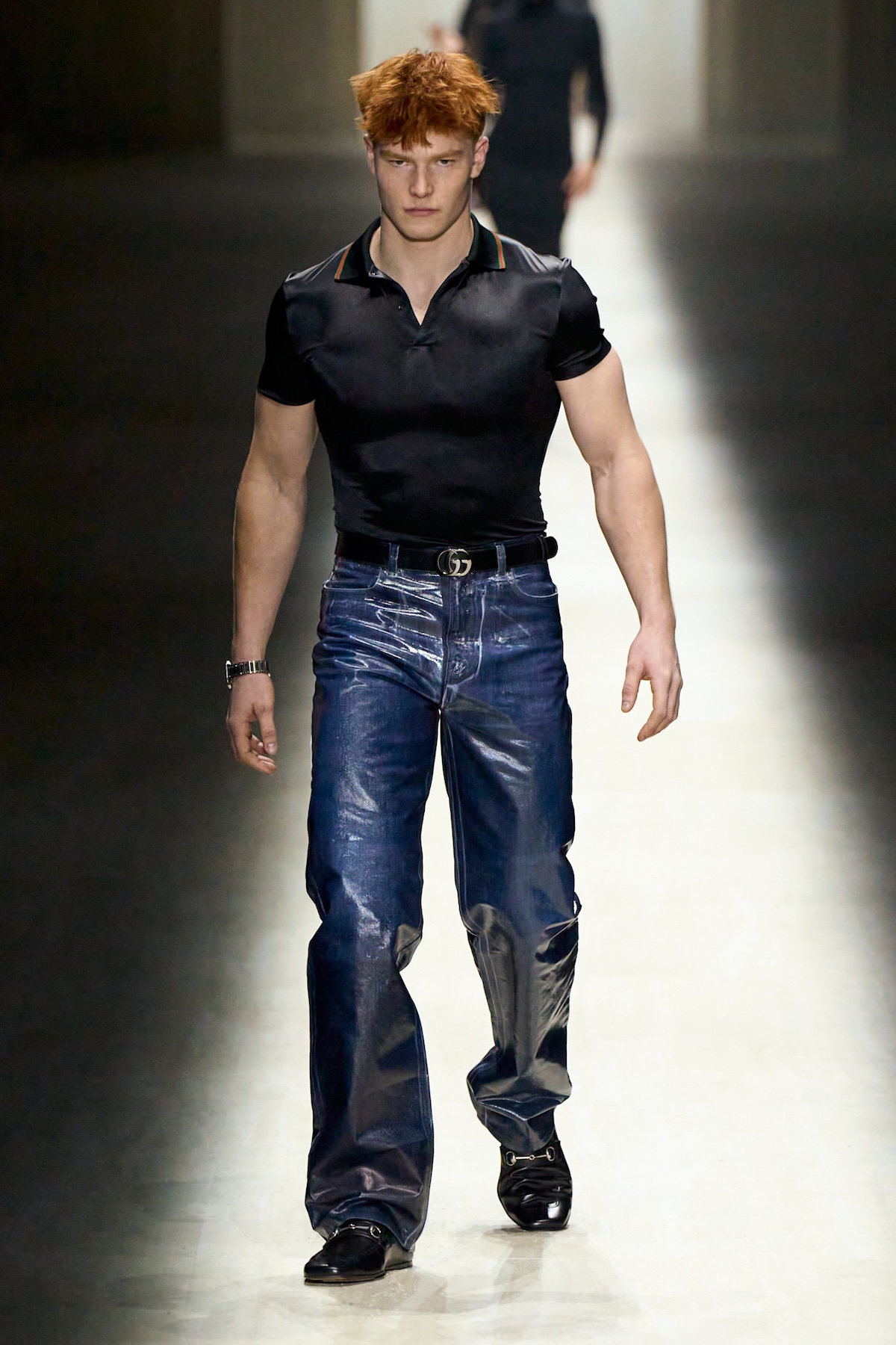 Модель чоловічої колекції Gucci у чорній футболці-поло та блискучих джинсах на подіумі Gucci