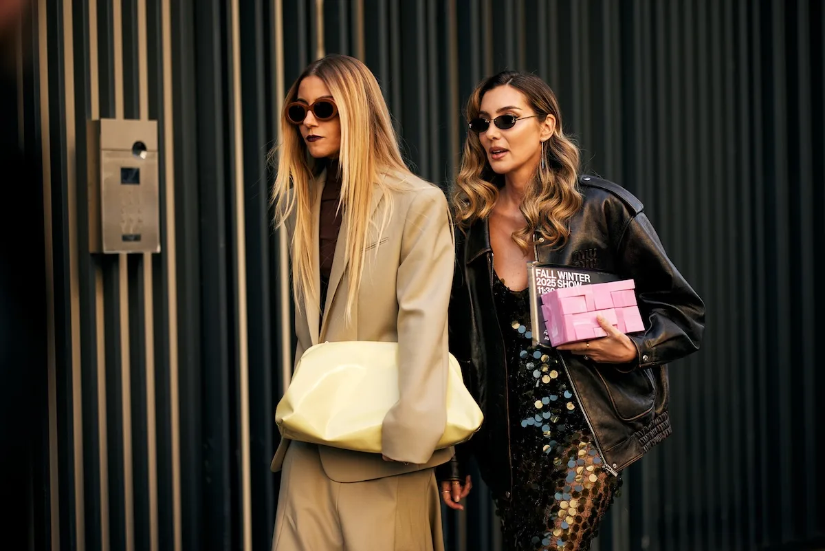 Чистий четвер, о котрій годині відкриваються магазини у 2026 році? З будівлі виходять дві стильно одягнені жінки в сонцезахисних окулярах, одна несе велику світлу сумку, інша — коробку з написом