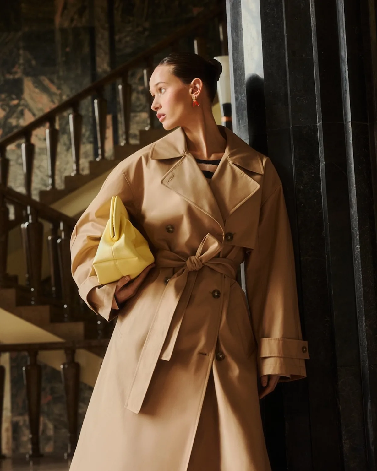Модель одягнена в класичний бежевий тренч, що підкреслює тенденцію до позачасової, більш преміальної пропозиції — відповідно до стратегічного розвитку сегмента вищого класу. Стиль, доповнений контрастною жовтою сумочкою, також відображає потребу привернути увагу клієнтів, що в контексті фінансових результатів пов'язане зі зростанням маркетингових витрат та боротьбою за продажі.