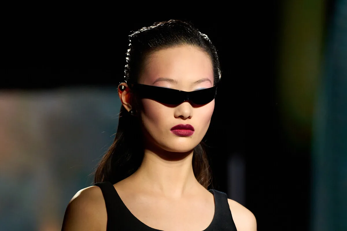 Модель на подіумі демонструє мінімалістичний, але водночас виразний макіяж — з яскравими губами та ніжним відтінком шкіри, доповненим футуристичними окулярами. Цей образ нагадує естетику аватарів Roblox, де макіяж часто поєднує простоту з особливим штрихом. Образ демонструє, як реальна мода та краса надихають на персоналізацію цифрових персонажів.