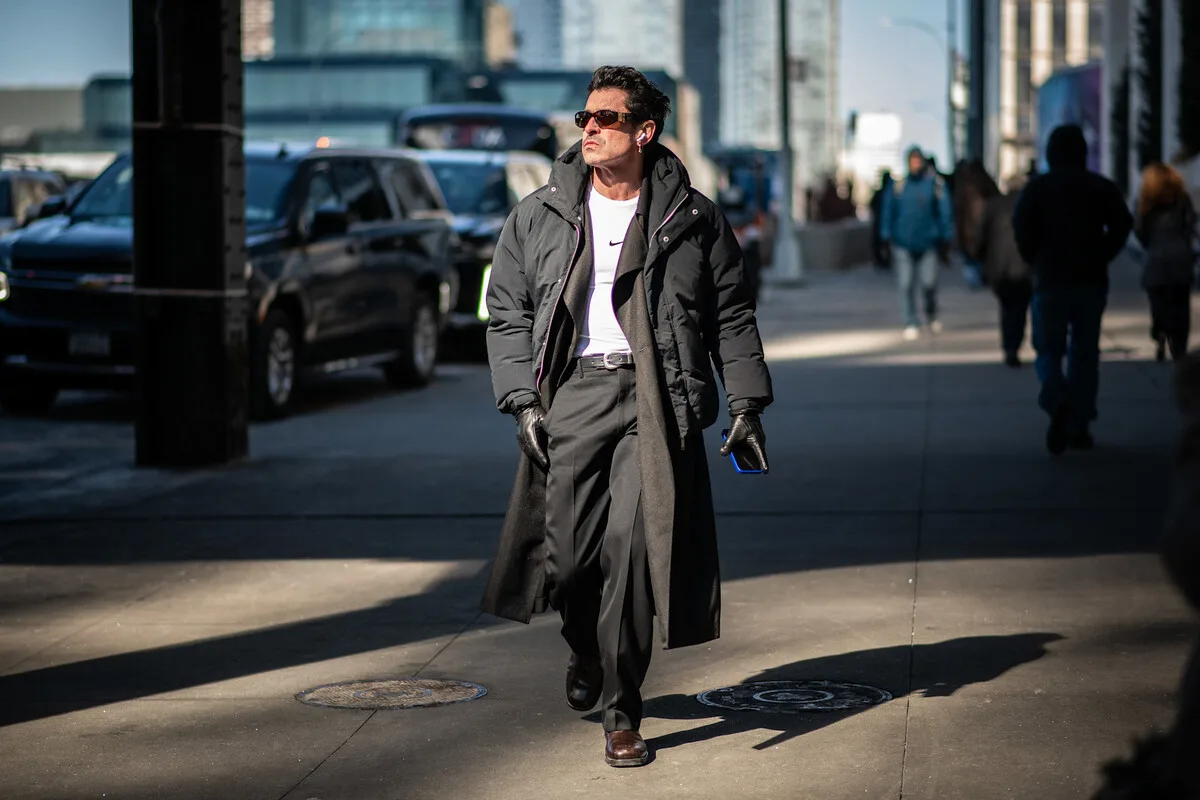 Управління з питань конкуренції та захисту прав споживачів (UOKiK) висунуло звинувачення у рекламі товарів Black Red White, Peek & Cloppenburg та Żabka Nano. Чоловік у темному пальто та сонцезахисних окулярах йде тротуаром у центрі міста, тримаючи в руках телефон. На задньому плані видно вуличний транспорт та перехожих, що підкреслює динамічне міське середовище. Фотографія є ілюстративною та натякає на тему комерції та щоденних покупок.