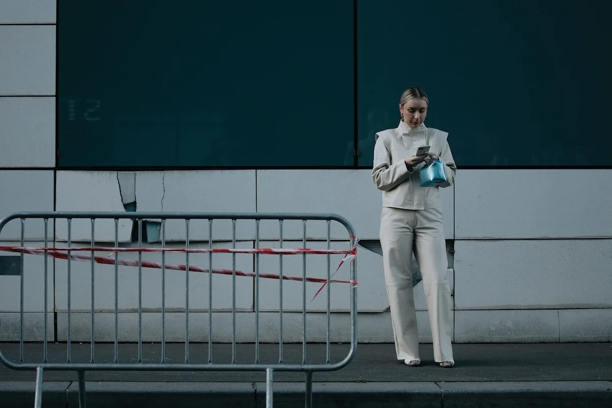 Жінка в яскравому вбранні стоїть поруч із сучасною будівлею та користується смартфоном. Зображення підкреслює щоденне використання технологій та контекст, у якому цифрові дані можуть стати об'єктом витоку.