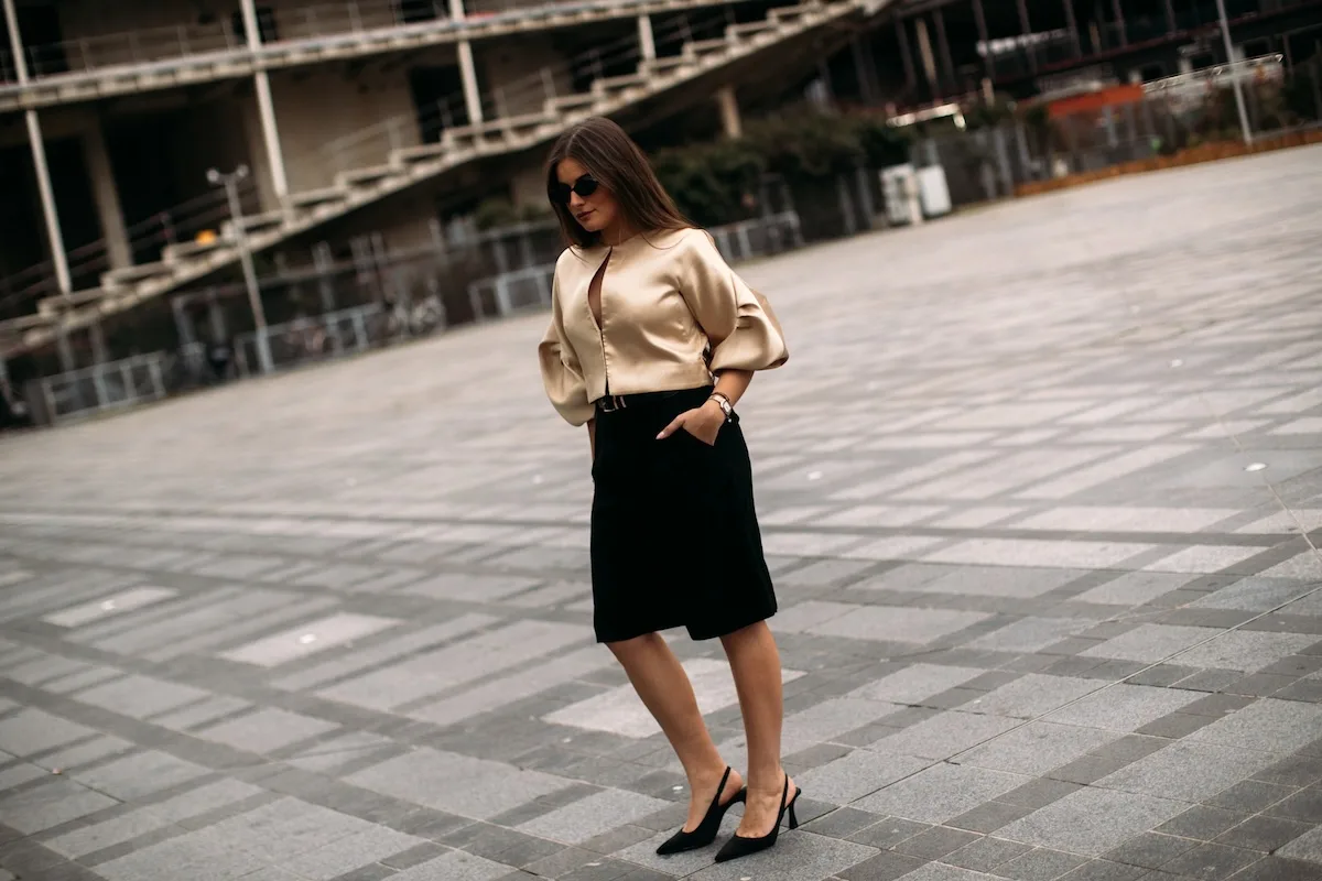 Елегантна жінка в бежевій блузці та чорній спідниці прогулюється сучасною площею в міському стилі. Цей класичний образ, ідеальний для робочого дня, показує, що навіть коли 2 травня не вихідний, можна виглядати стильно та професійно.