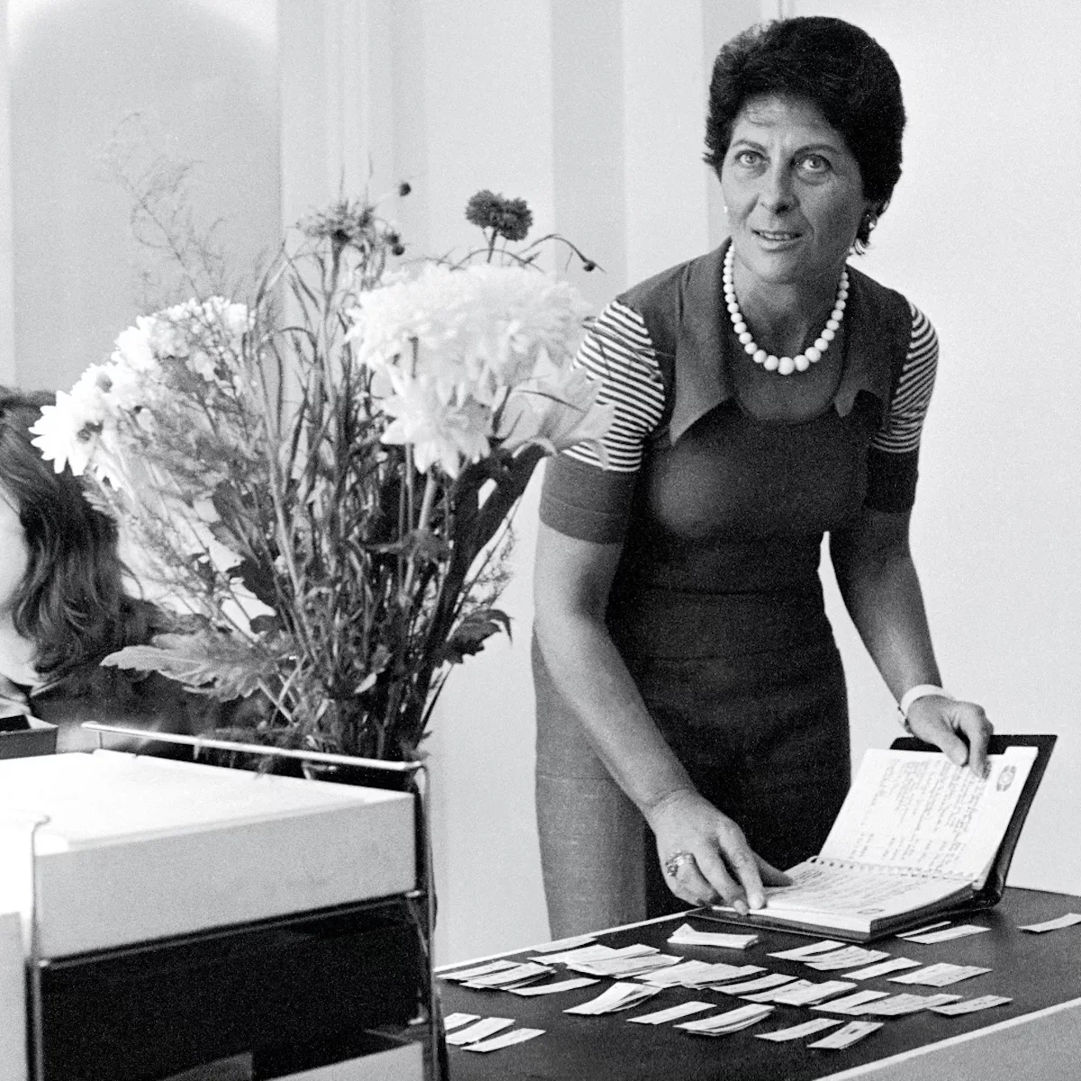 Чорно-біле фото Джоан Берштейн за роботою в бутіку Browns у Лондоні. Модельєрка та кураторка переглядає нотатки та обирає колекції — сцена, яка відображає її інтуїтивний підхід до відкриття нових талантів.