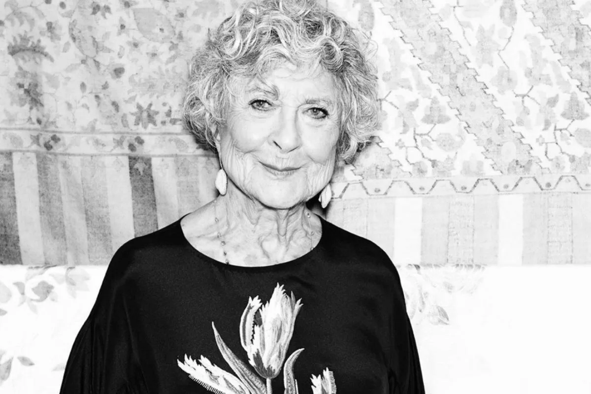 Чорно-білий портрет Джоан Берштейн, засновниці бутика Browns та однієї з найважливіших постатей в історії модної роздрібної торгівлі. Її елегантна фігура та спокійна посмішка відображають її самобутній стиль та багаторічний досвід у відкритті талантів у фешн-індустрії.