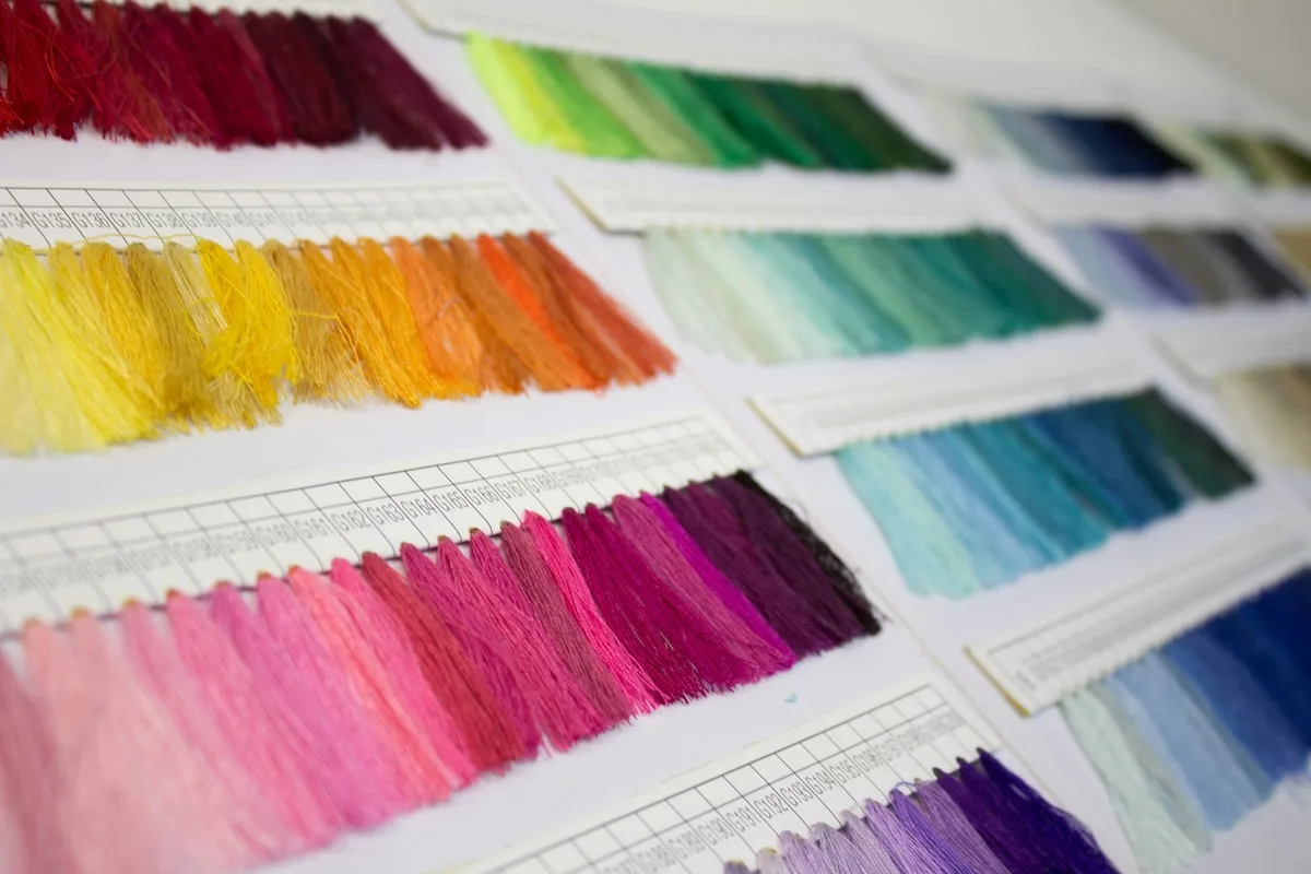 Зразки кольорових ниток, розташовані в палітрах, демонструють різноманітність кольорів, що використовуються у текстильному виробництві. Це фото ілюструє етапи проектування та підготовки матеріалів у швейній промисловості.
