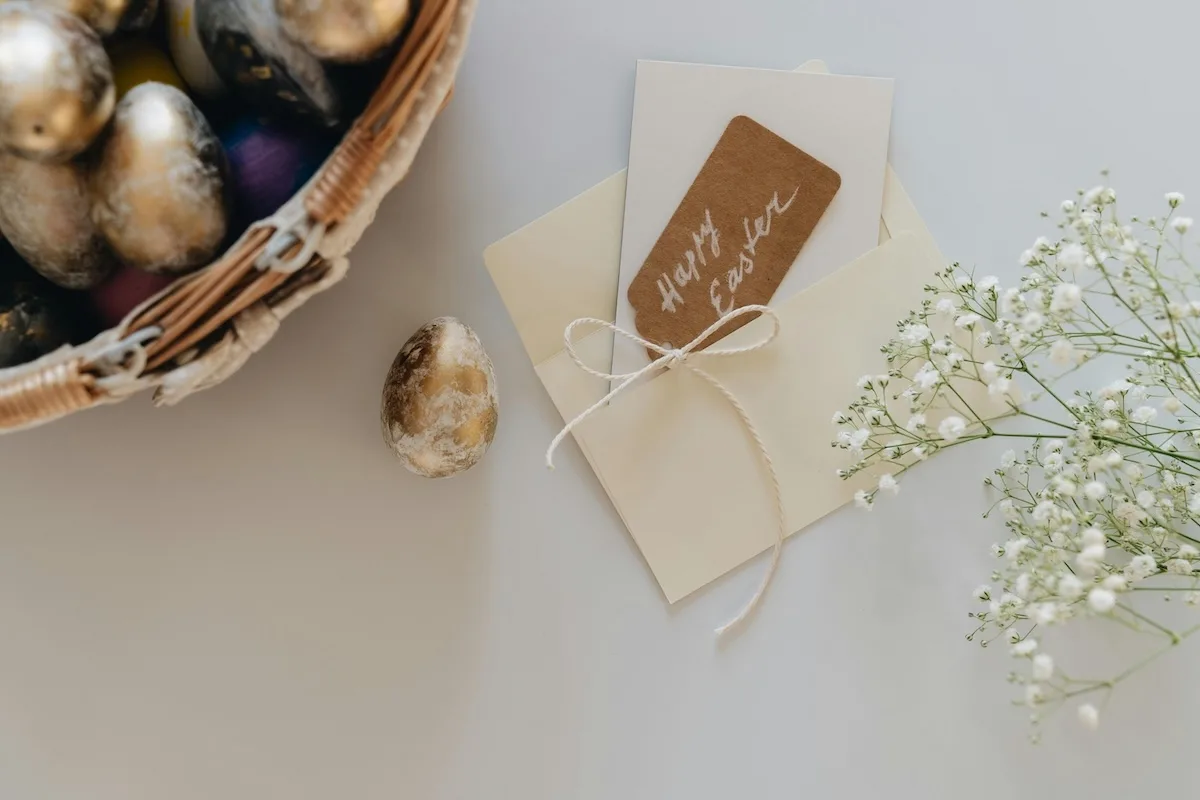 Елегантна великодня листівка з корпоративними привітаннями, пасхальним яйцем та весняними квітами на світлому фоні.