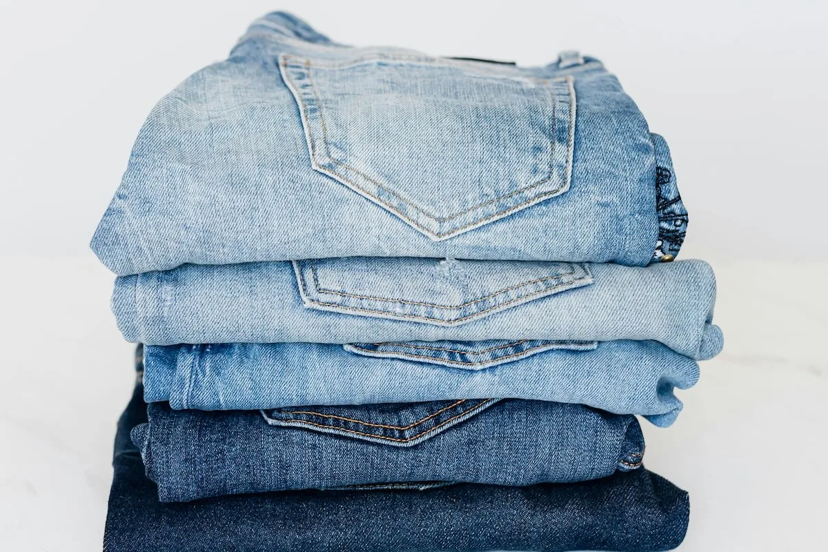 Стопка джинсів різних відтінків синього, складених одна на одну, з видом на задні кишені джинсових штанів.