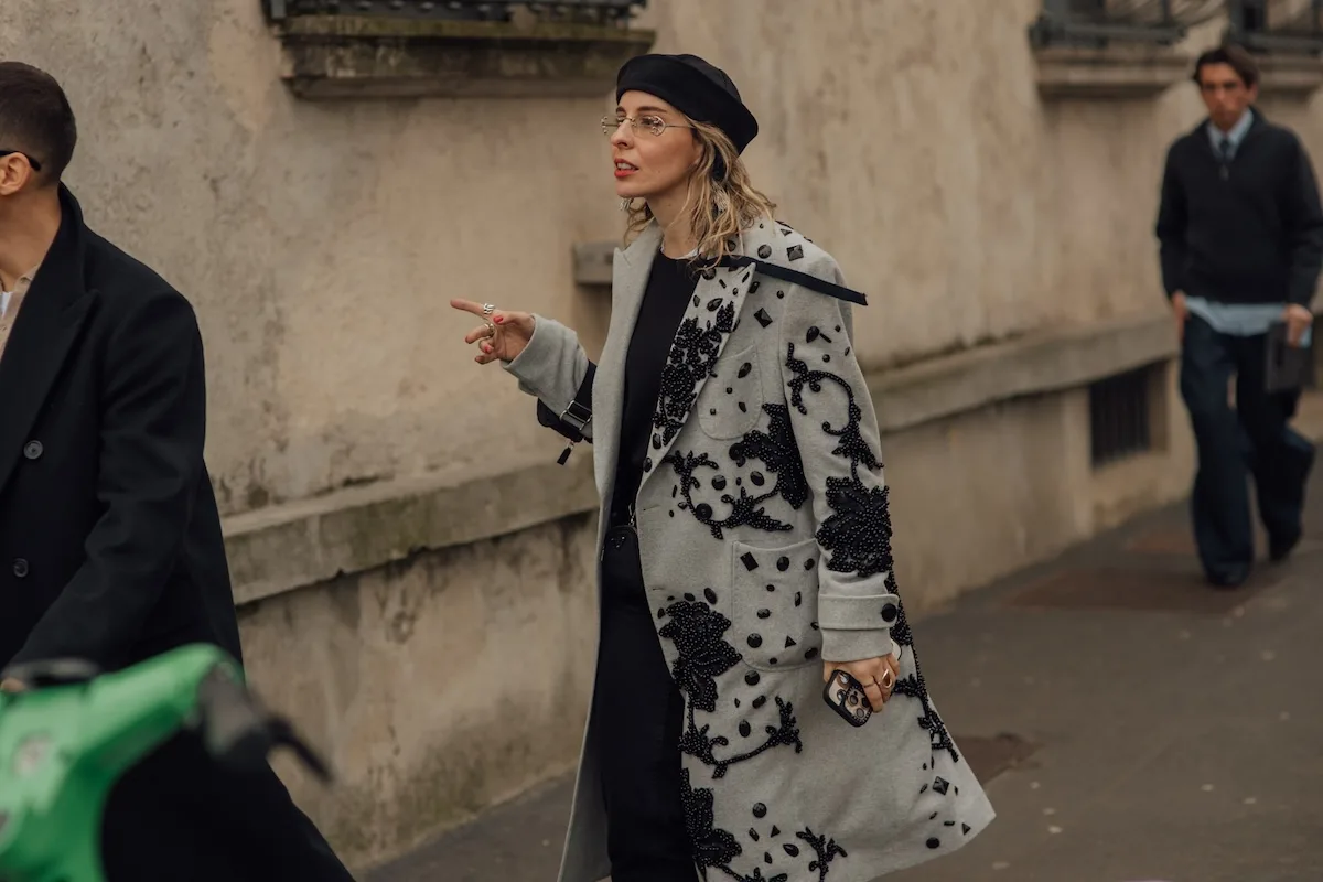 Жінка в елегантному пальто та береті йде вулицею та вказує рукою – сценка у міському вуличному стилі, ілюстративне фото.