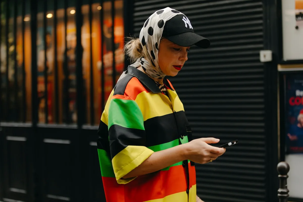 Жінка в яскравому вбранні користується смартфоном під час прогулянки містом. Фото ілюструє повсюдність мобільних пристроїв та зростаючу важливість безпеки даних у повсякденному житті.