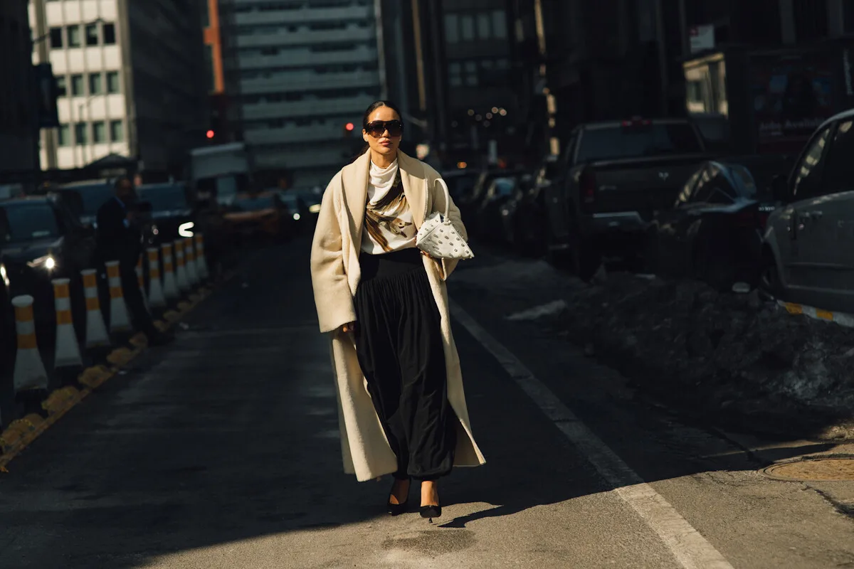 Зростання цін на одяг у 2026 році. Стильна жінка на вулиці в елегантному пальто підкреслює зміни на ринку моди на тлі зростання цін на одяг у 2026 році. Зростання витрат на виробництво та сировину дедалі більше спонукає споживачів обирати якість, а не кількість.