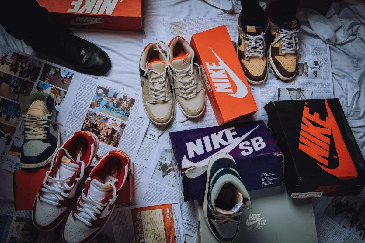 Nike подає до суду на клієнтів. На фото: Колекція взуття Nike виставлена поруч із культовими коробками з логотипом бренду. На фото зображено різні моделі спортивного взуття та кросівок на тлі газет та рекламних матеріалів.
