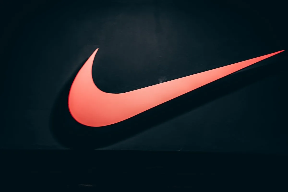Підсвічений логотип Nike на темному фоні. Компанія переживає глобальну реструктуризацію, яка включає закриття технологічного центру в Польщі та скорочення робочих місць у кількох країнах.