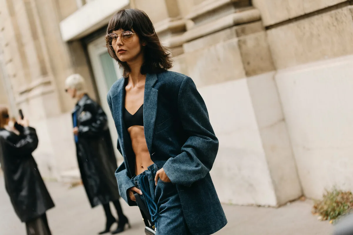 UOKiK H&M Peek & Cloppenburg. Жінка в темно-синьому вуличному вбранні позує на вулиці під час Тижня моди. Фото ілюструє тему акцій та цін у магазинах одягу, а також дії UOKiK проти відомих модних брендів.