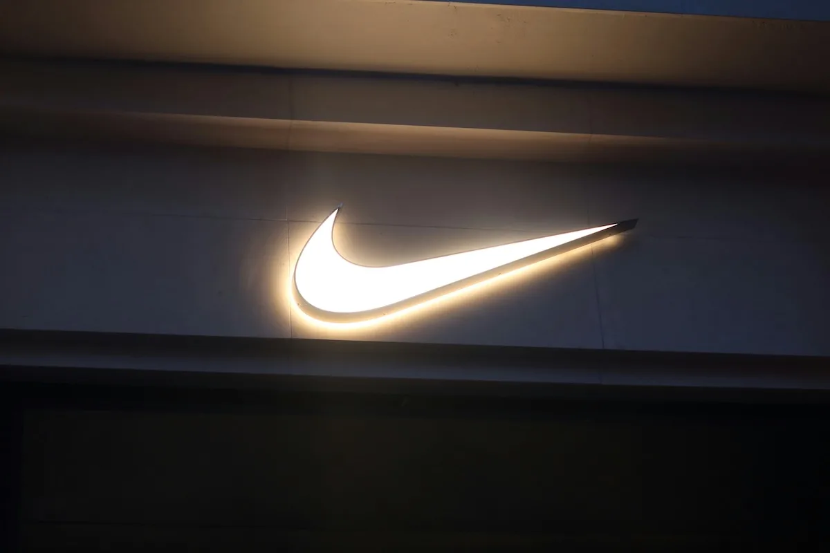 Підсвічений логотип Nike розміщено на фасаді спортивного магазину після настання темряви. Відмітний символ бренду виділяється на тлі темного фасаду будівлі.